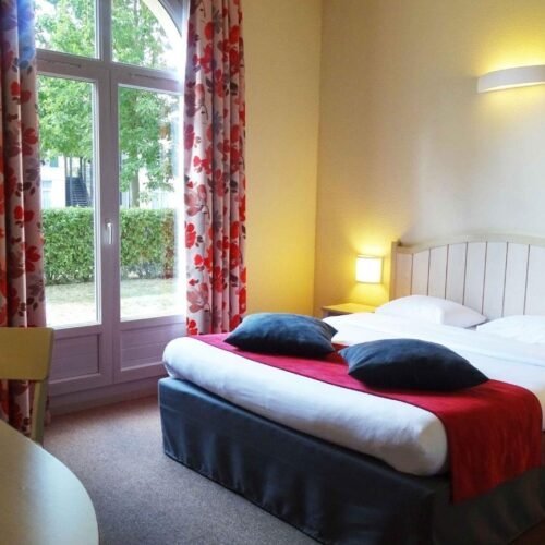 Tweepersoonskamer Campanile Weißes Doppelbett mit roter Tagesdecke und geblümten Vorhängen
