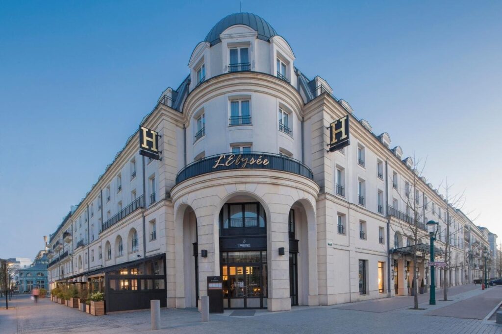 Weißes Gebäude Hotel l'Elysée Val d'Europe mit goldener Beschriftung und schwarzen Fensterrahmen