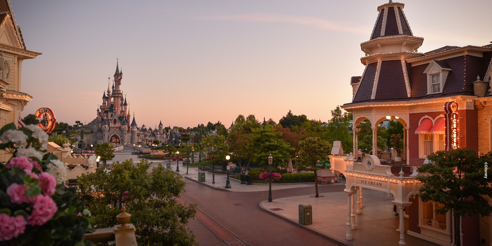 Mainstreet U.S.A.® mit Blick auf das Schloss von einem Balkon mit rosa und weißen Blumen im Disneyland® Park