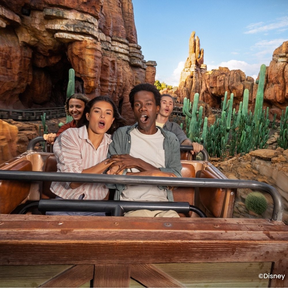 Menschen auf der Big Thunder Mountain-Achterbahn zwischen roten Felsen und Kakteen