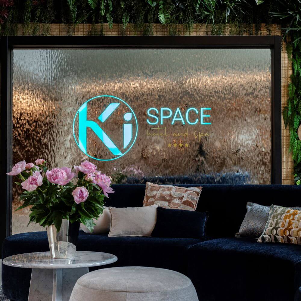 Donkerblauwe bank en witte tafeltjes met roze rozen voor een muur met het logo van Ki Space